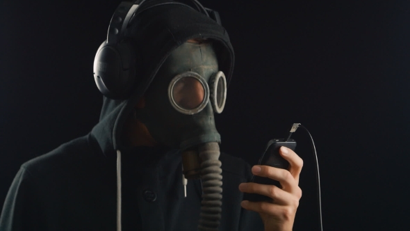 Man Listens To Music With Headphones With a Gas Mask Covering His Face.