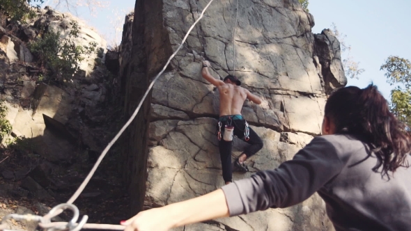 Man Climbing The Cliff With Woman Belaying Him