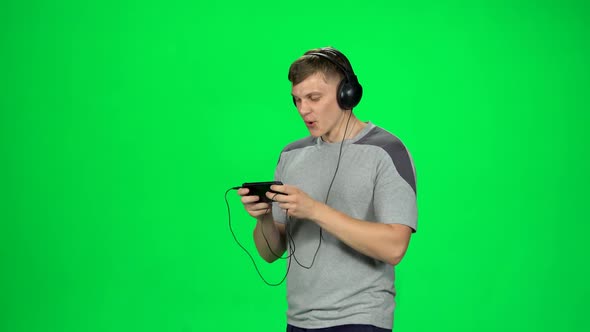 Funny Guy in Big Black Headphones Goes and Texting with Smartphone on Green Screen at Studio