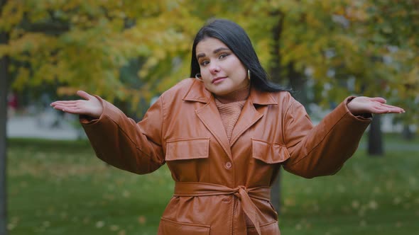 Young Puzzled Upset Hispanic Woman Standing Outdoors in Park Shrugging Shoulders Doubtful Looking at