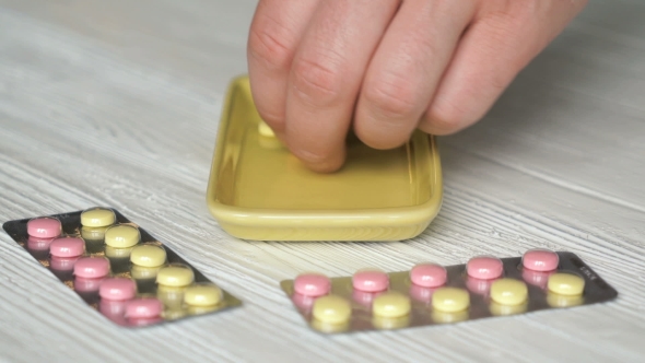 Hand Collects The Pills In a Yellow Container