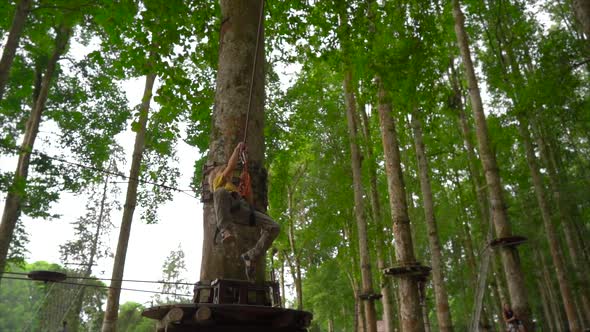 Slowmotion Shot of a Little Boy in a Safety Harness on a Zipline in Treetops in a Forest Adventure