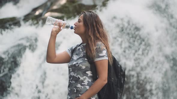 Attractive Girl Drinks Cold Water From a Bottle and Quenches Thirst While Standing on a Stone Near