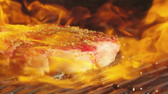 Ribeye steak cooking on a flaming grill.