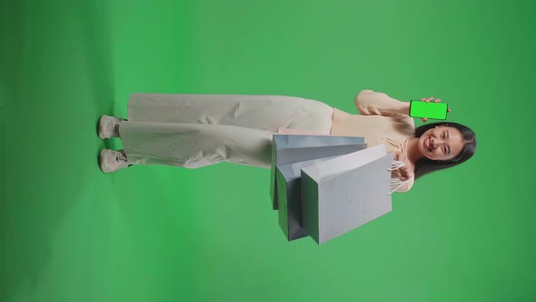 Full View Of Woman Holding Green Screen Mobile Phone And Shopping Bags In Front Of Green Screen