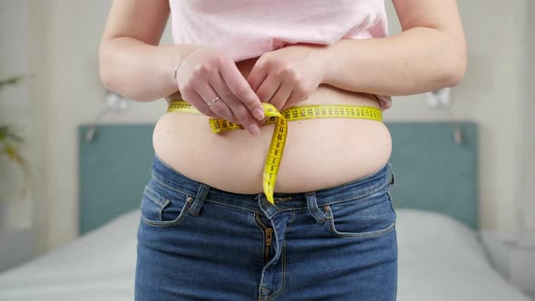 Young Woman Thinking of Loosing Weight Measuring Her Waist with Measuring Tape