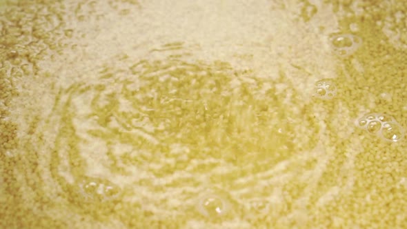 Cooking couscous. Falling dry yellow grains into water in slow motion. Close-up