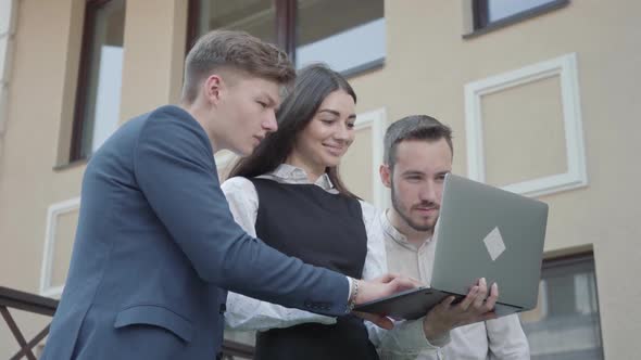 Young Woman and Two Men in Formal Wear Discussing Project on the Laptop on the Terrace. Business