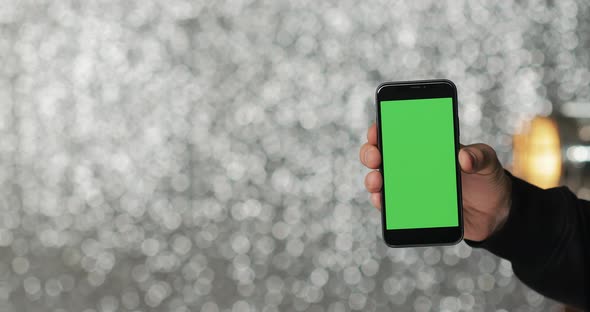 A Man's Hand Holding Green Screen Smartphone on the Silver Sequin Background
