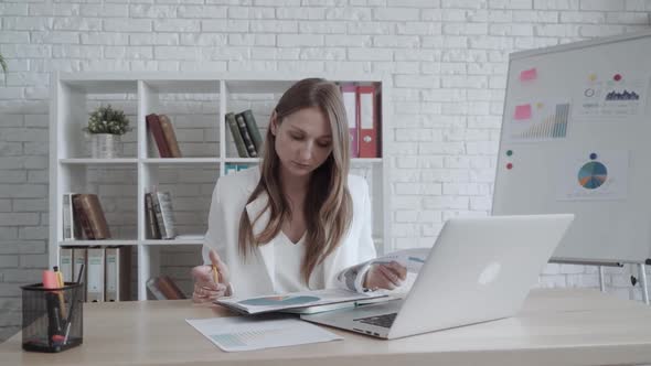 Beautiful Business Woman Looks Statistics While Sitting at Office Desk