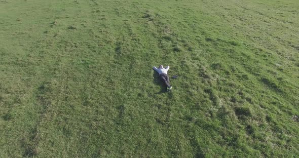 Low Orbital Flight Around Man on Green Grass with Notebook Pad at Yellow Rural Field