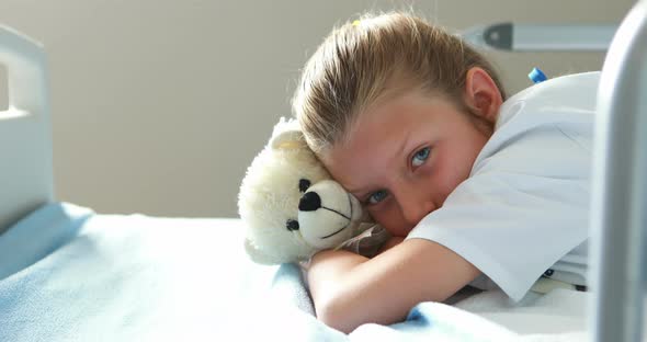 Sick girl lying with teddy bear on bed