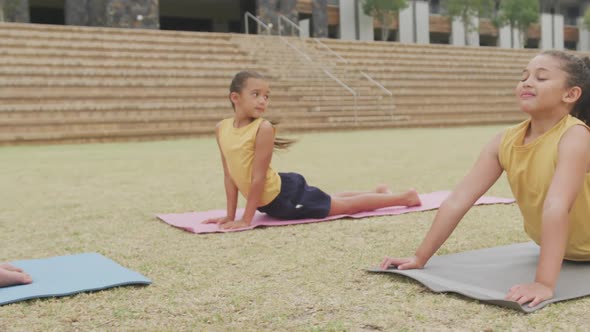 Video of focused diverse girls practicing yoga on mats in front of school