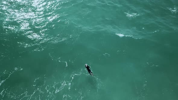 Surfer swimming through choppy waves. Zooming out drone shot.