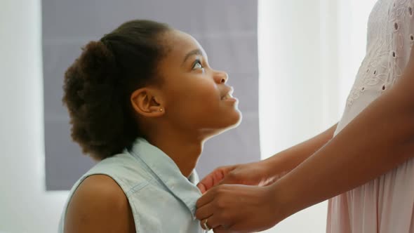 Side view of mid adult black mother helping her daughter in wearing dress in a comfortable home 4k