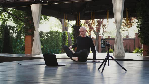 Yoga Instructor in Black Sportswear is Sitting in Lotus Position and Looking at Laptop