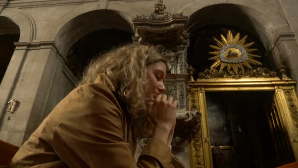 Faithful Woman Prays in Catholic Church with Eyes Closed Sitting on Bench