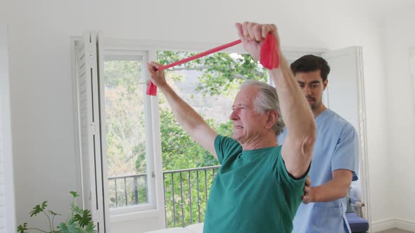 Slow motion of senior man exercising with resistance band by male physiotherapist at retirement home
