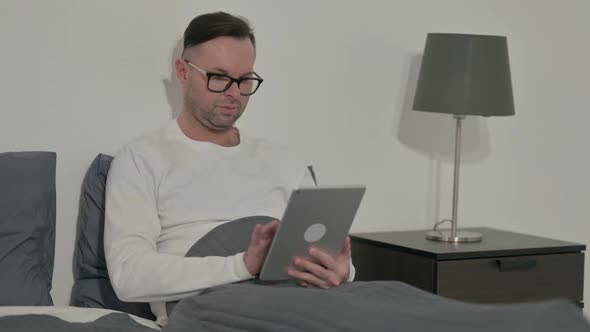 Casual Man Using Tablet While Sitting in Bed