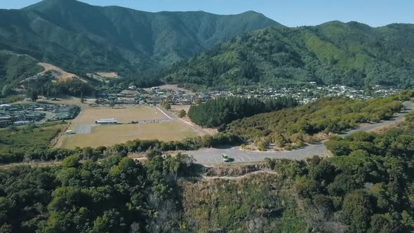 Aerial drone footage of a van on top of a hill near trees and mountains in Picton, New Zealand.