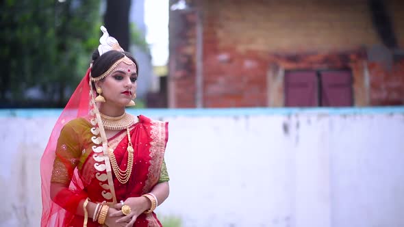 Thoughtful Indian Bengali Bride smiling and waiting outdoor wearing red saree