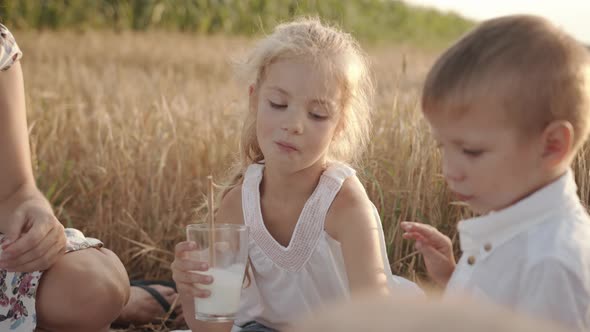 A Cute Preschool Girl Sits Next to Her Younger Brother at a Family Picnic in a Wheat Field and Pours