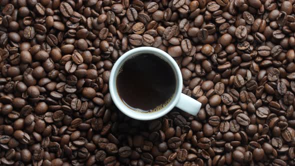 White cup of hot coffee and rotating background of fresh roasted coffee beans