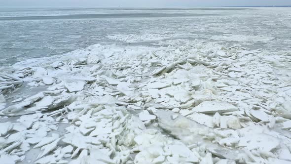 Drone flying backwards over sheet of melting ice on lake. Miniture iceburgs melting on water with li