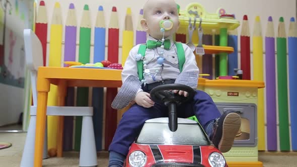 Little Boy in a White Shirt in a Red Toy Car at Home