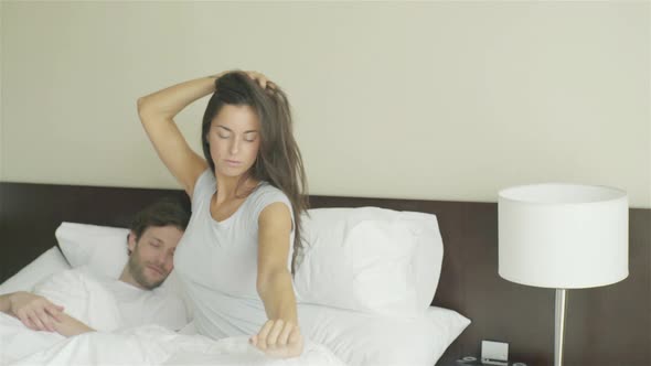 Woman waking up in bed next to sleeping husband