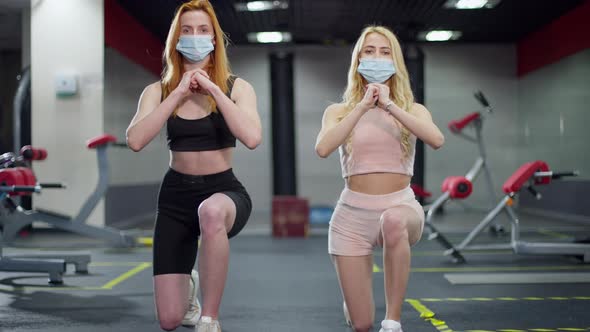 Front View of Two Sportswomen in Coronavirus Face Masks Doing Lunges in Gym