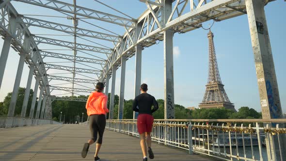 A man woman couple running across a bridge with the Eiffel Tower