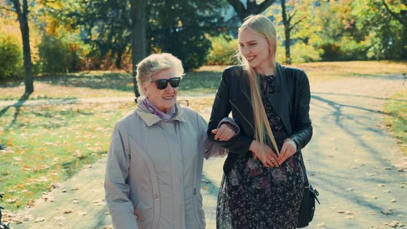 Old Woman Walking Together with Cheerful Blonde Girl in Autumn Park