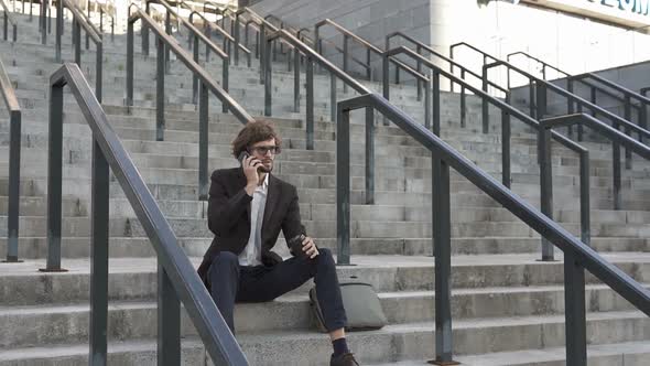 Businessman Sitting on Stairs Near Business Center Talking on the Phone