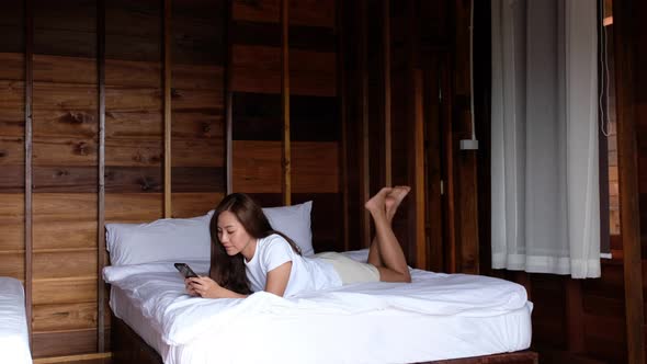 A beautiful asian woman lying down on the bed, using mobile phone before sleeping