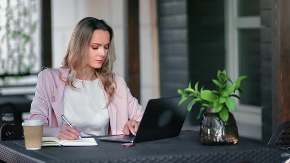 Focused Business Freelancer Blonde Woman Working Remotely at Street Cafe Use Laptop Making Notes alt