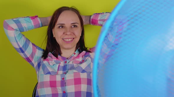 Close Up of Young Woman Sitting on Chair in Front of Fan on Yellow Background