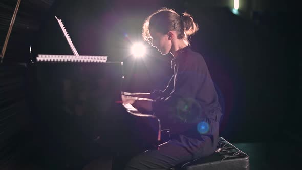 A young woman plays the piano energetically in the spotlight on the stage