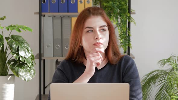 Thoughtful concerned red hair female student working on laptop looking away thinking solving problem