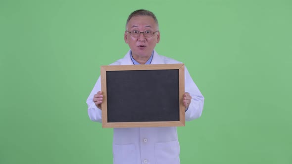 Happy Mature Japanese Man Doctor Looking Surprised While Holding Blackboard