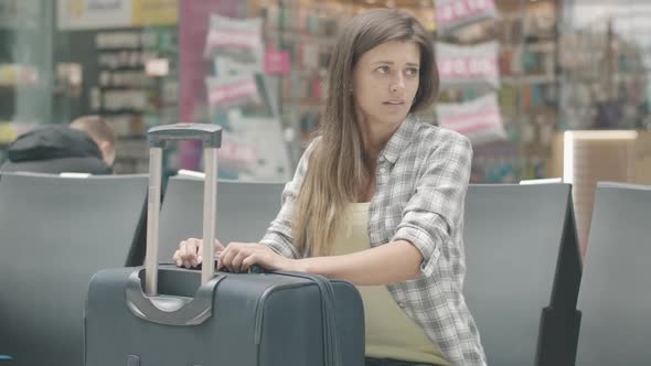 Portrait of Bored Young Caucasian Woman Sitting with Baggage in Waiting Area. Brunette Tourist Wait