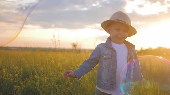 Little Boy in the Sunset Catches Soap Bubbles in Meadow. Relax with Child in Nature. Soap Bubble