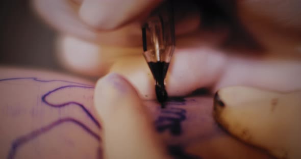 Tattoo artist making a text tattoo drawing on a person's hand, macro shot