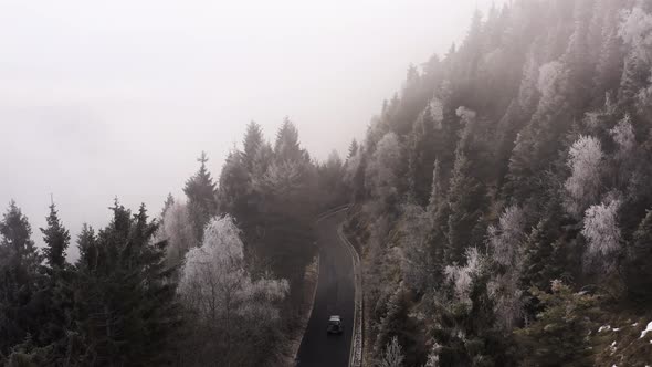 Aerial View of a Car Driving in a Foggy Day in Mountain. Car Driving in a Curved Road with Near