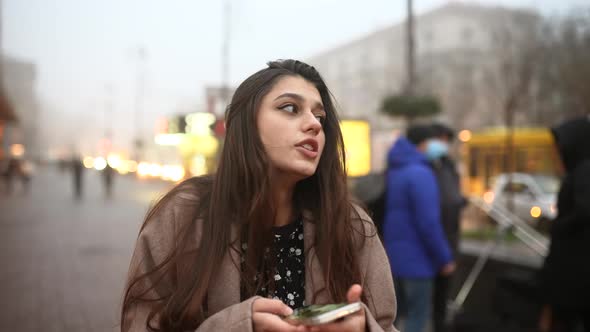 Young Woman Walking Down the Street and Typing in Her Mobile Phone