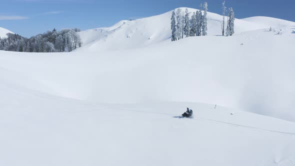 People Riding on Snowmobile with Snowboard on Snowy Highlands Sunny Winter Day