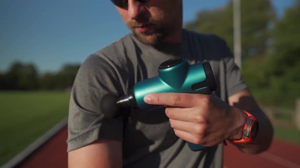 An Athlete Massages with a Percussion Therapy Gun to Relieve the Pain of Muscle Aches After a