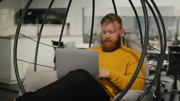 Man Using Laptop Working Sitting In Egg Chair At Workplace