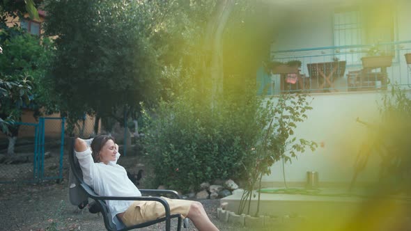 A Young Woman Enjoying Fresh Air While Sits in an Armchair in the Garden