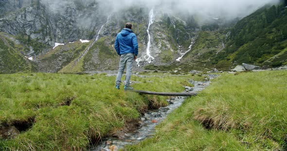 Hiker or Backpacker Trekking in the Mountains Standing in Front of Alpine Valley with Waterfall